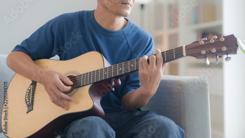 фотографія A man playing an acoustic guitar while sitting comfortably on a sofa in a bright