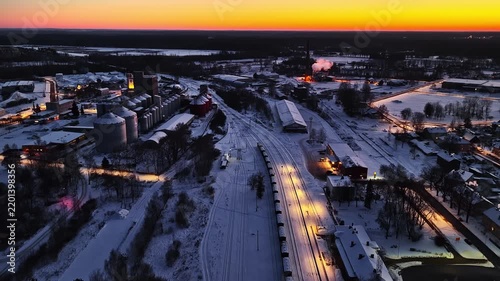 Drone flying over a snow-covered town with an industrial factory and railway at dusk