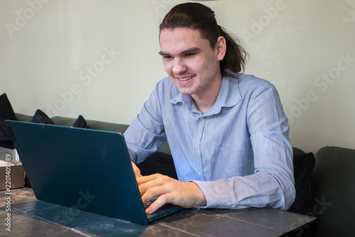 A young man sits at a cafe table focused on his laptop. He has a cup of coffee beside him.