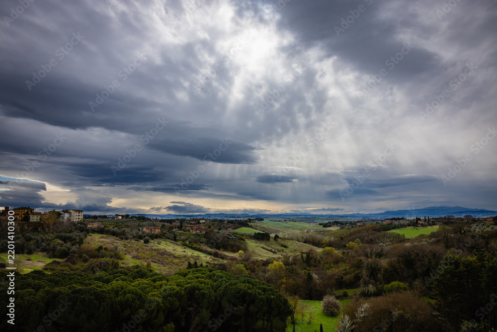 Obraz premium Sun rays breaking through dramatic clouds over Tuscan hills