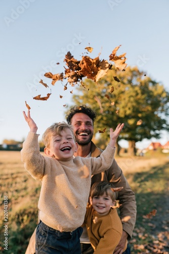 Happy father with two children tossing autumn leaves outdoors on a countryside walk for seasonal background