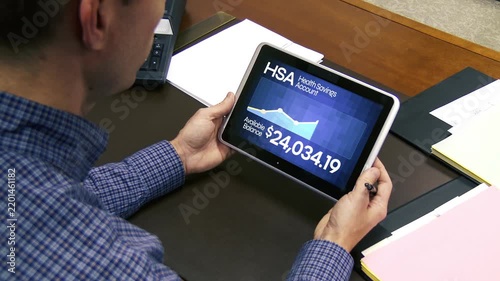 Man reviews his Health Savings Account balance and financial information on a tablet while sitting at a desk. 15426