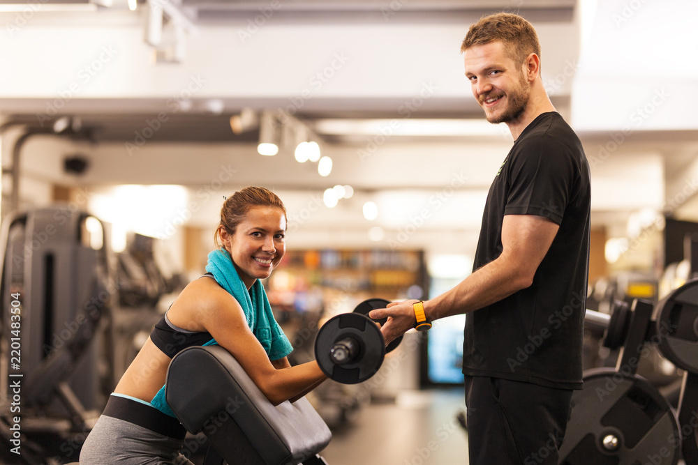 Fototapeta premium happy girl posing with fitness coach lifting weights