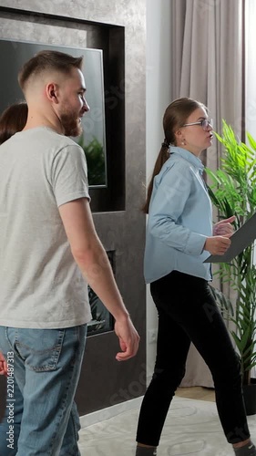 Vertical video. Real-estate agent showing family spacious house. Young couple entering modern apartment they are going to buy. Realtor talking to clients.