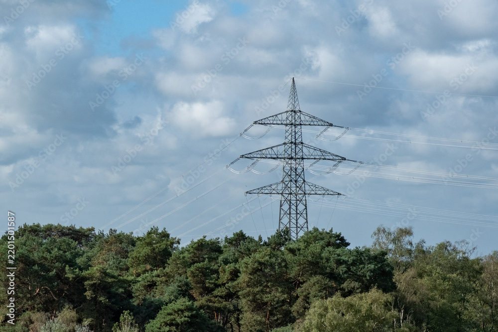 Obraz premium Electricity pylon stands tall among trees under blue sky with clouds