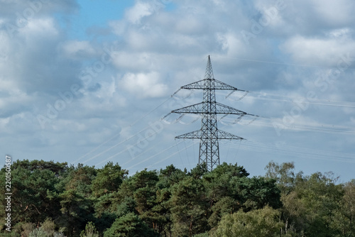 Quadro su tela Electricity pylon stands tall among trees under blue sky with clouds
