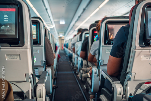 The image captures passengers seated in an airplane cabin, showcasing the rows of seats and individual screens. The atmosphere inside the aircraft is calm, with travelers settled for their journey.