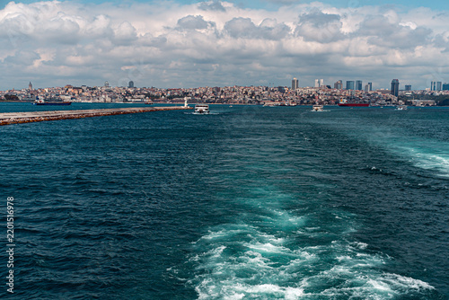 The photo captures a vibrant scene of the Bosphorus Strait, with boats navigating its deep blue waters. Istanbul's skyline forms a picturesque backdrop under a partly cloudy sky.