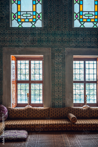 This photo captures an elegant Ottoman interior featuring intricate stained glass windows and richly patterned seating. The vibrant colors and detailed design evoke a sense of historical luxury.