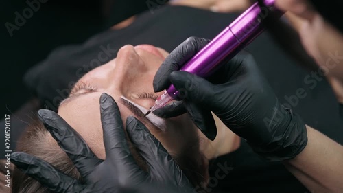 Permanent makeup artist performs an eyebrow tattoo procedure after mapping the shape, creating natural brows with a PMU machine in a professional beauty studio.