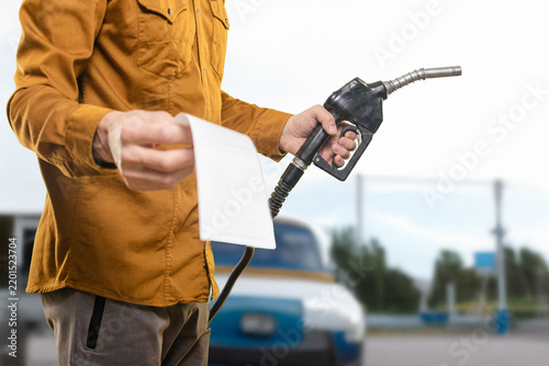 Closeup photo of man holding bill while refueling car at gas station Checking the fuel receipt to verify refueling costs and payment details
