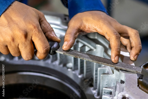 A mechanic uses a hand file tool to smooth a metal component.