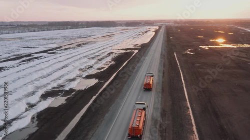 Shooting from a drone. Fuel trucks carry gasoline to remote parts of the country. Special tank cars driving along the highway among snow-covered fields in a deserted area. Fuel delivery in a crisis.