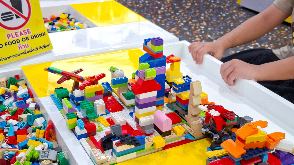 Obraz premium Child hands building colorful lego city towers and plastic brick structures on yellow play table at indoor playground on September 22, 2026 in Bangkok, Thailand.