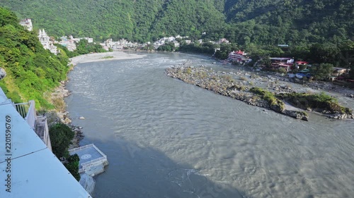 A broad bend of the Ganga River opens toward wooded hills and a distant settlement in Rishikesh.
