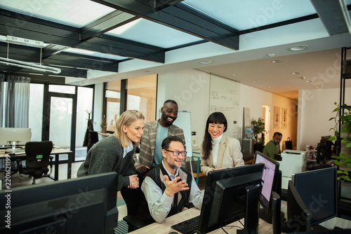 Coworkers gathered around computer in modern office