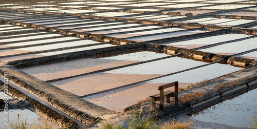 Wooden bench resting beside peaceful salt evaporation ponds at sunrise.