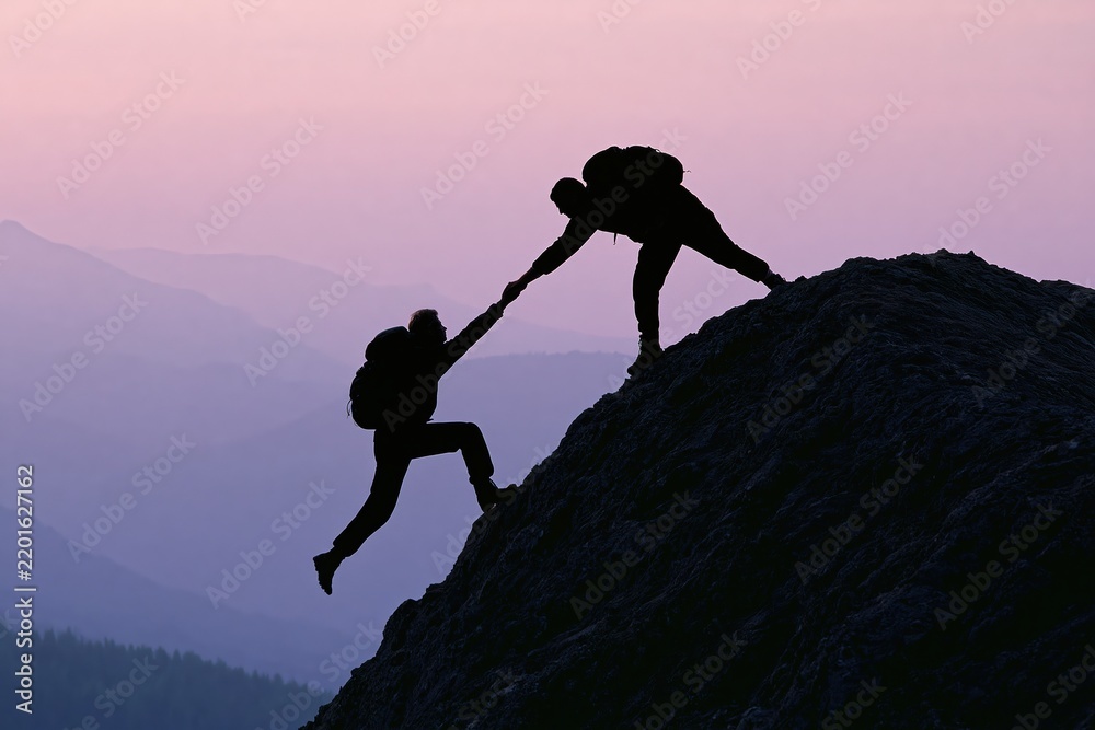 Obraz premium Silhouette of two hikers helping each other climb a mountain at sunrise