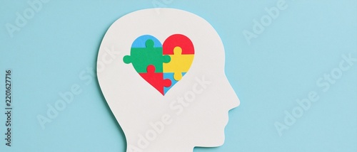Human head silhouette with colorful puzzle heart symbol on blue background