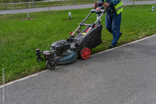 Worker mowing grass edge with petrol lawnmower along park pathway. Lawn maintenance and landscaping concept. Real Photo