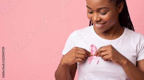 Smiling woman wearing pink ribbon on white shirt against pink background for breast cancer awareness portrait