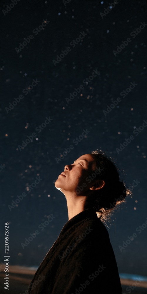 Fototapeta premium Woman silhouette looking up at a starry night sky for contemplative background and peaceful poster design