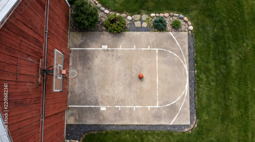 Aerial view of a rustic basketball hoop on barn with a concrete court in a backyard during a sunny day