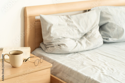 Bild auf Leinwand Cozy, leisurely morning ritual in bright bedroom: cup of coffee, an open book, and glasses on wooden nightstand, soft natural light, and comfortable unmade bed