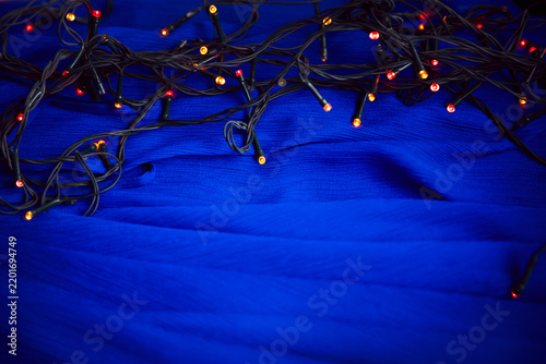 Christmas string lights on blue fabric background close up