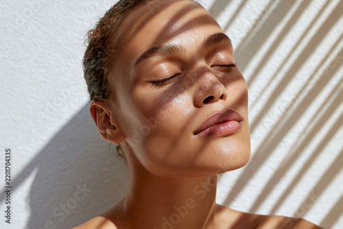 Young woman basking in sunlight with eyes closed and patterned shadow across face