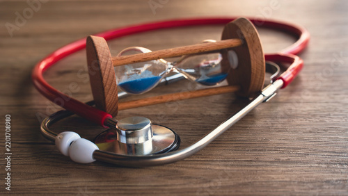 Vintage Sand Hourglass Timer Resting Inside Red Stethoscope Loop on Wooden Desk Concept for Emergency Care, Medical Response Time, and Health Urgency