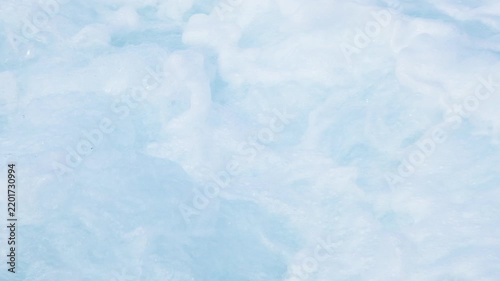 Turquoise ocean waves swirling with white sea foam, creating a dynamic natural water texture and abstract marine background. Slow motion video.
