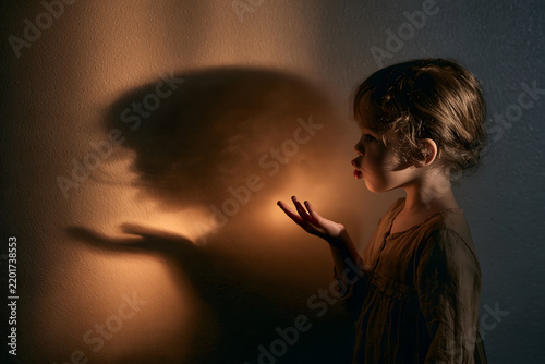 The silhouette of a playing child is cast against a wall bathed in warm light.space on the side for text.a faint warm glow suggesting candlelight bleeding into the shadow's edge
