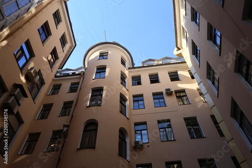 Well courtyard enclosed by beige apartment buildings; a modern glass-paneled structure juts into the frame, contrasting with historic architecture