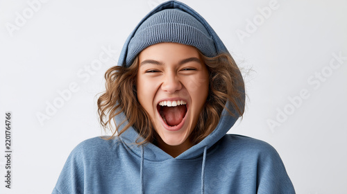 Joyful young woman in a blue hoodie and beanie shouting happily with a wide open mouth.