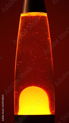 Glowing Orange Lava Lamp with Floating Yellow Wax Bubbles Against Red Background, Retro Psychedelic Mood Lighting