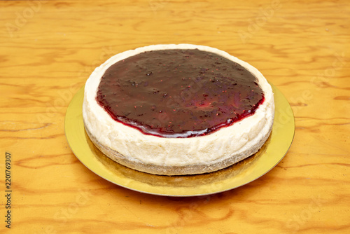 Obraz na płótnie Whole round cheesecake topped with glossy mixed berry compote, set on a gold cake board over warm wooden surface