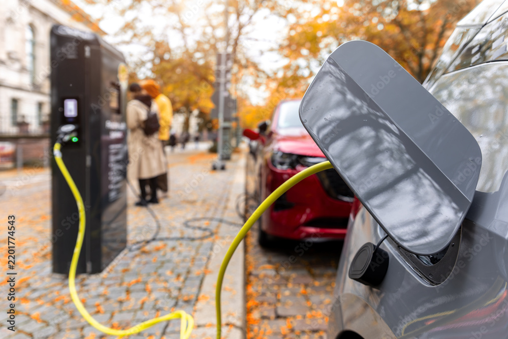 Obraz premium Electric car charges at station, highlighting shift from oil dependence toward clean mobility. EV charging symbolizes energy crisis, fuel scarcity, sustainability, electrification, and transition
