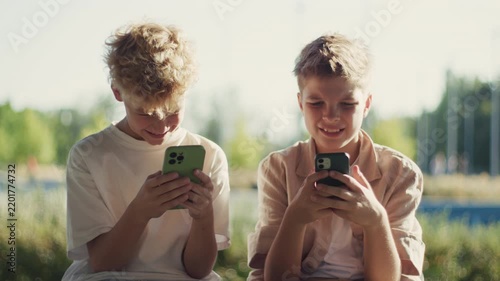 Two Boys Smiling While Using Smartphones Outdoors