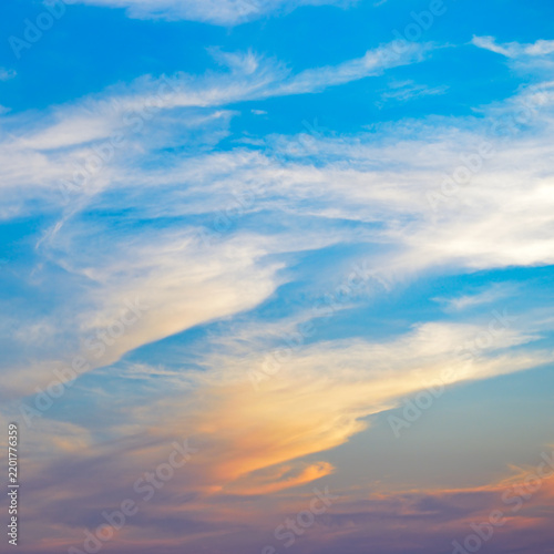 Dramatic evening sky with light white clouds and warm sunbeams reflecting on a clear blue horizon