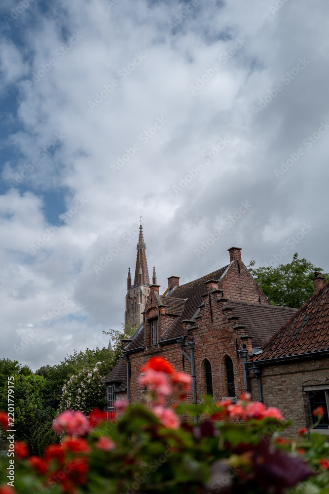 Fototapeta premium Bruges church spire and brick buildings with flowers
