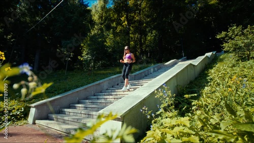 Young woman jogging pose on concrete stairway in forest park under bright sunlight and green foliage