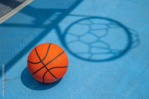 Basketball on blue court with hoop shadow
