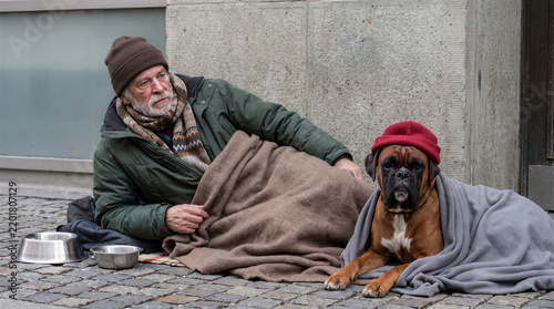 Senior homeless man resting on city street in winter with his loyal boxer dog wrapped in blankets