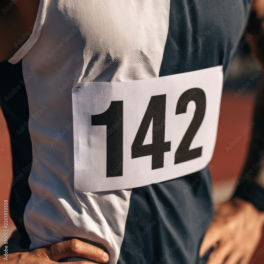 Naklejka premium A race participant shows their marathon bib with the number 142. The event takes place outdoors with runners preparing to start.