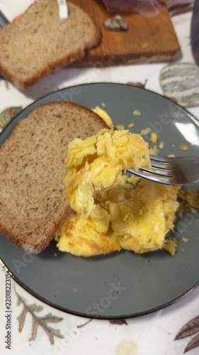 Fork lifting scrambled eggs beside slices of bread