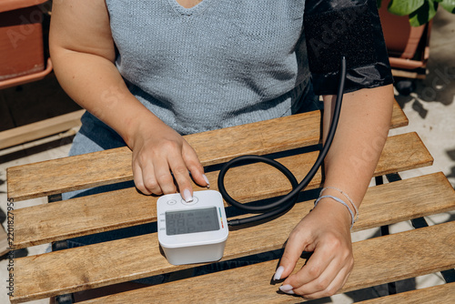 Woman Checking Blood Pressure at Home With Digital Arm Cuff Monitor on Wooden Table