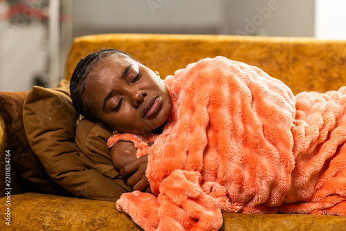 Foto African woman feeling sick having fever and headache, sleeping on a sofa wrapped