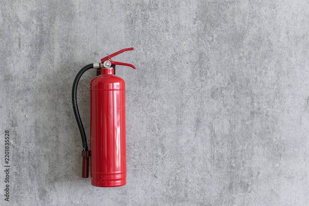 Fototapeta premium The Red Fire Extinguisher Mounted on a Rough Concrete Wall in Warehouse