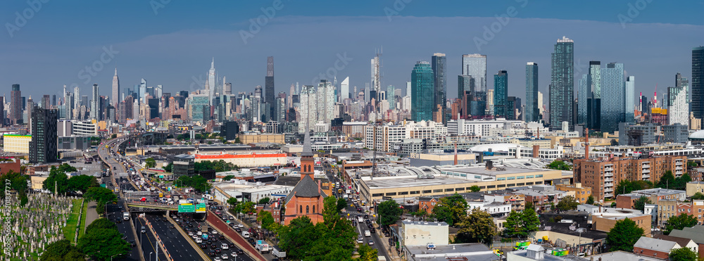 Fototapeta premium Aerial perspective displays traffic on the expressway in Queens leading toward towering skyscrapers of Midtown Manhattan under a clear daytime sky in New York.